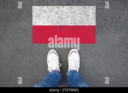Immigrazione. Uomo in piedi su asfalto vicino alla bandiera della Polonia, vista dall'alto Foto Stock