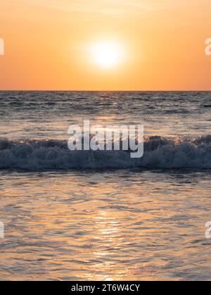 Una vista mozzafiato di un tramonto dorato su un oceano calmo mentre le onde dolci si infrangono sulla riva Foto Stock