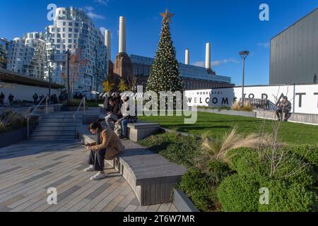 Persone sedute di fronte alla centrale elettrica di Battersea con Prospect Place appartamenti residenziali di lusso sullo sfondo. Londra , Regno Unito. Foto Stock