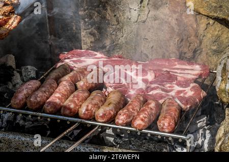 Cucinare bistecche, costolette e salsicce su un grande barbecue con fuoco di legno Foto Stock