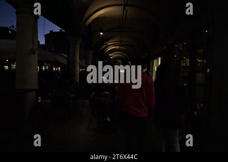 Mantova, Italia - ottobre 2023 - Porchway con persone sedute ai tavoli di un caffè vicino a una piazza al tramonto Foto Stock