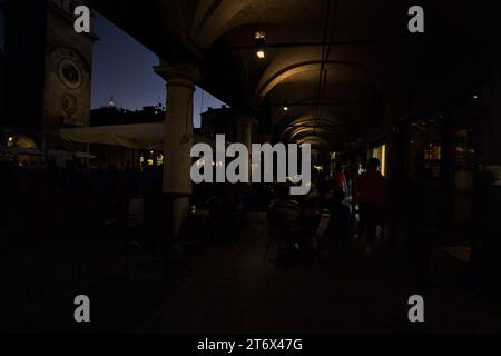 Mantova, Italia - ottobre 2023 - Porchway con persone sedute ai tavoli di un caffè vicino a una piazza al tramonto Foto Stock