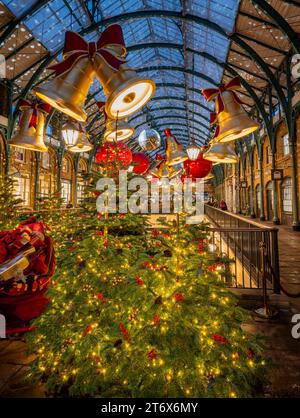 Londra, Regno Unito - 8 novembre 2023: Mercatino di Covent Garden con alberi di Natale e decorazioni natalizie. Campane e baule grandi pendono dal tetto. Foto Stock