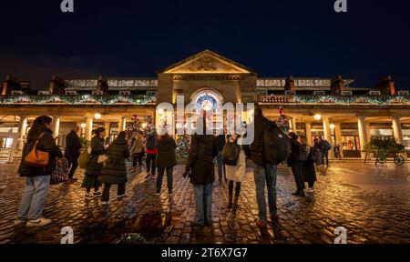 Londra, Regno Unito - 8 novembre 2023: Persone che ammirano gli alberi di Natale e le luci fuori dal mercato di Covent Garden. Foto Stock