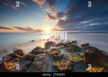 Splendido paesaggio nuvoloso sul mare e sulla costa rocciosa all'alba Foto Stock