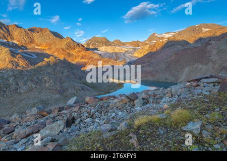 Alba sul ghiacciaio Malavalle e piccolo stagno alpino sottostante, montagne dorate all'alba sulle Alpi italiane. Foto Stock