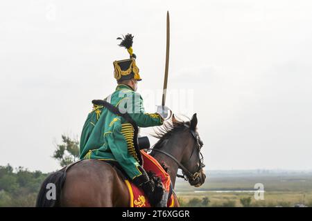 Un ussario in uniforme verde cavalca con una sciabola disegnata in mano durante una rievocazione storica della battaglia. Pakozd, Ungheria - settembre 30. 2023. Foto Stock