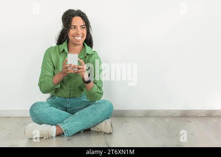 Signora nera che sorride mentre invia messaggi al cellulare in casa Foto Stock