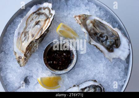 Le ostriche fresche a metà del guscio vengono servite in un piatto con ghiaccio, limoni e salsa. Il concetto di nutrizione sana. Foto Stock