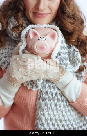 Ciao inverno. Primo piano su un'elegante donna di mezza età con maglione, guanti, cappello e sciarpa isolati su sfondo bianco con salvadanaio. Foto Stock