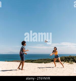 Giovani coppie multiculturali che giocano a pallavolo sulla spiaggia Foto Stock