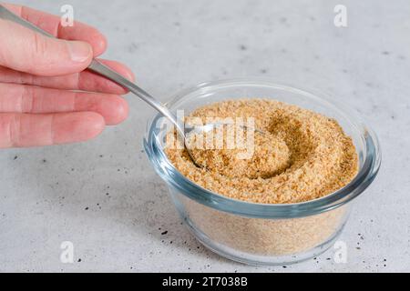 Cucchiaio di pasto di semi di lino in primo piano in mano di una donna, sfondo grigio chiaro, spazio per copiare Foto Stock