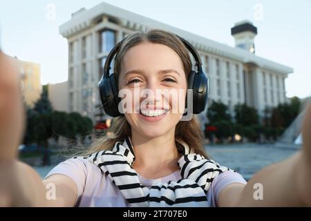 Donna sorridente in cuffie che scatta selfie per strada Foto Stock