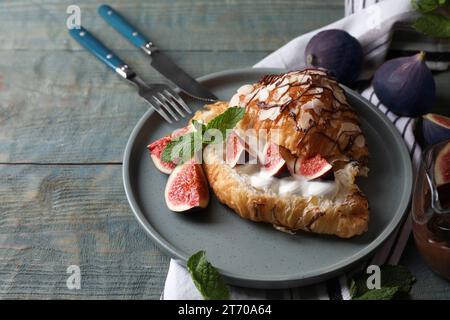 Deliziosi croissant con fichi e panna serviti su un tavolo di legno blu chiaro Foto Stock