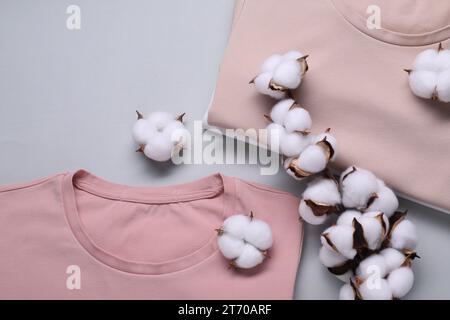 Rametto di cotone con fiori soffici e t-shirt su sfondo grigio chiaro, piatto Foto Stock