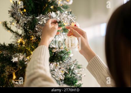 Immagine ravvicinata di una donna che decora un albero di Natale con un bellissimo ornamento, appesa una palla di Natale su un albero di Natale. speciale concetto di vacanza Foto Stock