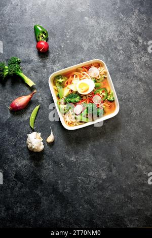 Zuppa vegetariana di noodle udon in ciotola su sfondo nero con ingredienti intorno Foto Stock