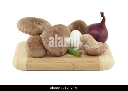 Funghi shiitake freschi, cipolle varie su un tagliere di legno isolato su sfondo bianco. Ricette di funghi ed erbe medicinali Foto Stock