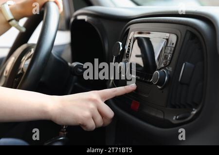 Scelta della radio preferita. Donna che preme il pulsante sull'audio del veicolo in auto, primo piano Foto Stock