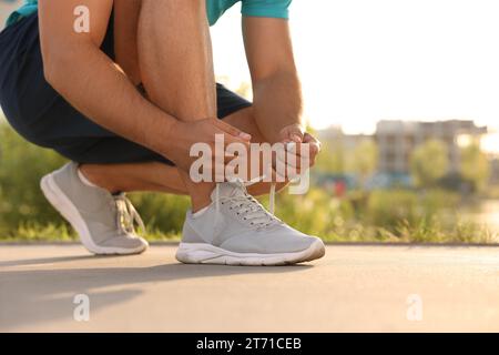 Uomo che stringe le scarpe prima di correre all'aperto nelle giornate di sole, primo piano. Spazio per il testo Foto Stock