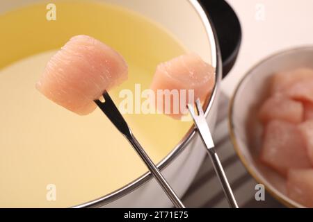 Pentola di fonduta con olio, forchette e pezzi di carne cruda su tavolo bianco, primo piano Foto Stock