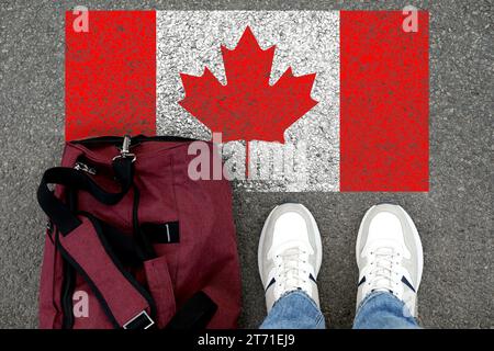 Immigrazione. Uomo con borsa in piedi sull'asfalto vicino alla bandiera del Canada, vista dall'alto Foto Stock