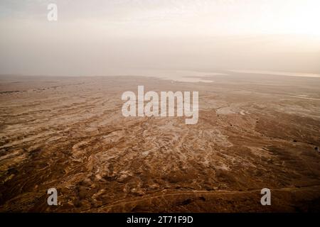 Vista aerea della costa del Mar morto senza vita contro il cielo grigio nebbioso all'alba. Mare salato, Israele. Superficie in terracotta della costa e mare bianco Foto Stock