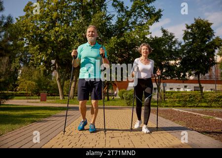 Felice coppia in pensione che si sta allenando con la pole walk nel parco pubblico urbano Foto Stock
