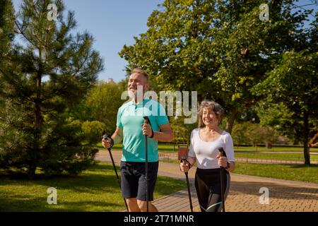 Felice coppia in pensione che si sta allenando con il Pole Walk in un parco urbano Foto Stock