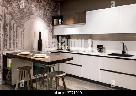 Design interno di cucina moderna arredata con armadi in legno bianco, piano lavabo con rubinetto nero, elettrodomestici moderni tavolo da pranzo con sgabelli Foto Stock