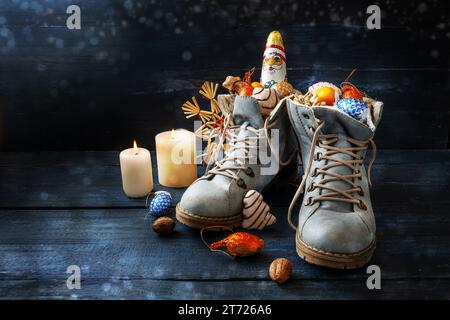 Tradizione sul German Nikolaus Tag che significa giorno di Nicola, le scarpe sono piene di dolcetti, qui stivali con dolci e decorazioni natalizie su legno blu scuro Foto Stock