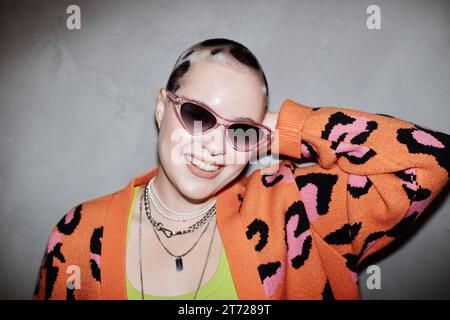 Ritratto di una giovane donna sicura di sé con stampe di ghepardi che indossa occhiali da sole e sorride alla macchina fotografica in studio Foto Stock