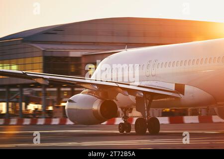 Aereo all'aeroporto affollato. Aereo passeggeri in movimento contro l'edificio del terminal alla bella alba. Foto Stock