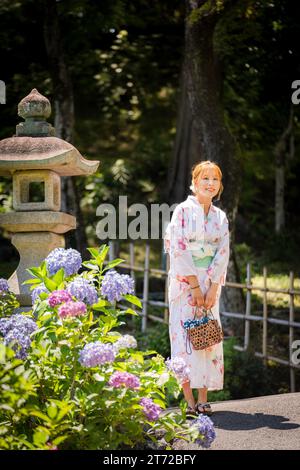 Ritratto di una giovane donna che indossa un kimono estivo yukata giapponese in un giardino di ortensie. Kyoto, Giappone. sfondo con sfocatura morbida. Foto Stock