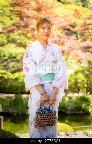 Ritratto di una giovane donna che indossa un kimono estivo yukata con sfondo morbido sfocato in un giardino giapponese. Kyoto, Giappone. Foto Stock