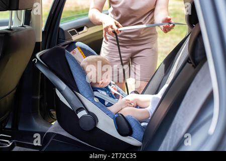 Una giovane madre mette il bambino su un seggiolino per auto e allaccia le cinture di sicurezza. Sicurezza dei neonati durante la guida. Primo piano Foto Stock