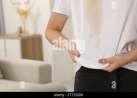 Donna che mostra macchie di caffè sulla camicia al chiuso, primo piano. Spazio per il testo Foto Stock