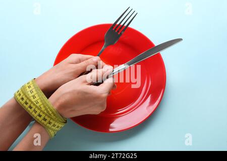 Concetto di dieta. Donna che tiene posate in mano legata con un metro a nastro su una piastra vuota su sfondo azzurro, vista dall'alto Foto Stock