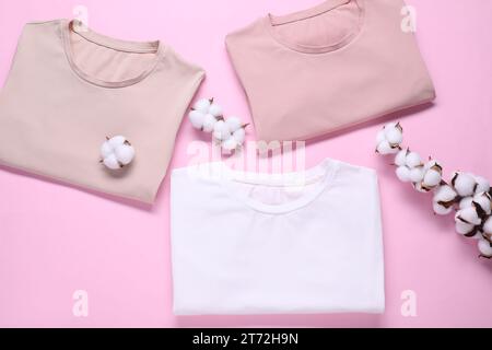 Rametto di cotone con fiori soffici e t-shirt su sfondo rosa, piatto Foto Stock