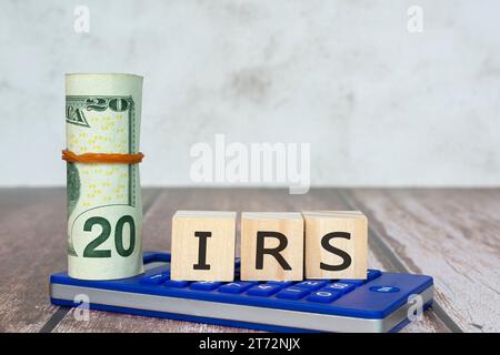 IRS Text IRS - servizio entrate interno su blocchi di legno con bolletta in dollari e calcolatrice su tavolo in legno. Foto Stock