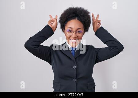 Bella donna africana con capelli ricci che indossa una giacca da lavoro e occhiali in posa divertente e pazza con le dita sulla testa come orecchie di coniglio, cheerfu sorridente Foto Stock