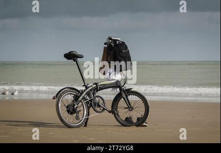 Bicicletta bilanciata su un banco, su una spiaggia di sabbia vuota, con due gabbiani e un paio di scarpe da ginnastica. Carrero Crosscity, E.. Foto Stock