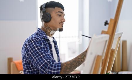 Ritratto di un giovane latino tatuato, un artista impegnato nel suo disegno, ascoltando un audio stimolante con le cuffie nel suo studio d'arte Foto Stock