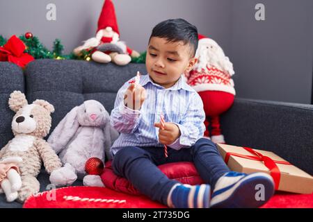 Adorabile bambino ispanico che sembra decorato con stelle di natale seduto sul divano a casa Foto Stock