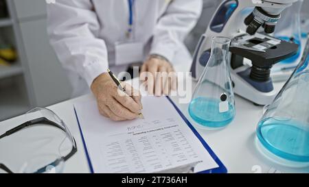 Mani meticolose di una donna scienziata, immersa in importanti ricerche, prendendo appunti con diligenza nel vivace laboratorio Foto Stock