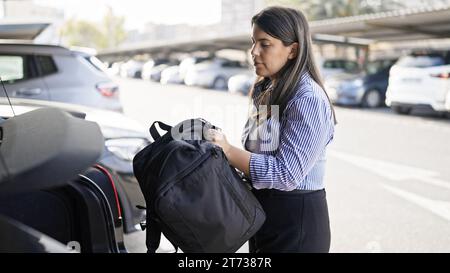 Giovane bella donna ispanica che apre il bagagliaio dell'auto e mette i bagagli nel parcheggio Foto Stock