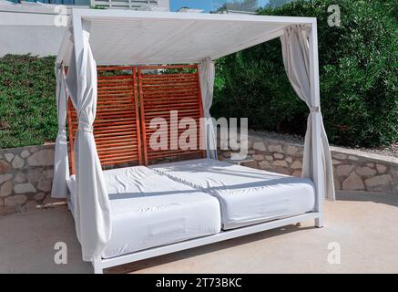 Letto a baldacchino bianco posizionato sulla terrazza di un lussuoso resort costiero. Il letto bianco contrasta splendidamente con le sfumature naturali dell'environ costiero Foto Stock