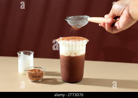 Mani versando la polvere di cacao alla bevanda con crema di latte al cioccolato, bevanda asiatica, spazio per i testi Foto Stock