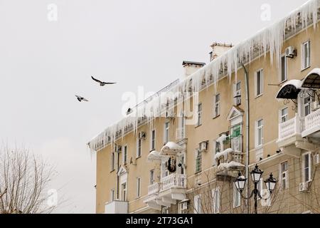 Enormi pezzi di ghiaccio appesi alle grondaie di edifici che minacciano di crollare durante il disgelo Foto Stock