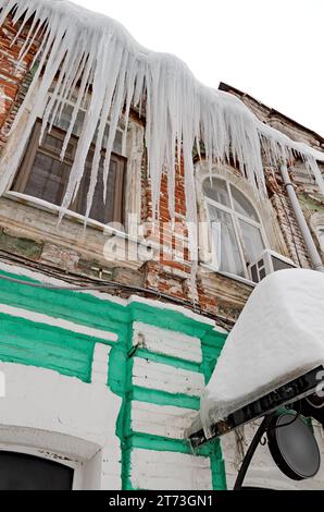 Enormi ghiaccioli affilati pendono pericolosamente dal tetto di una vecchia casa. Foto Stock